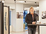 Ein Mann steht im Verkausraum vor Türen und hält einen Querschnitt eines Fensters